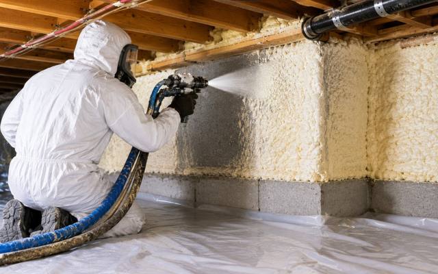 Installer spraying foam along a foundation wall and sill